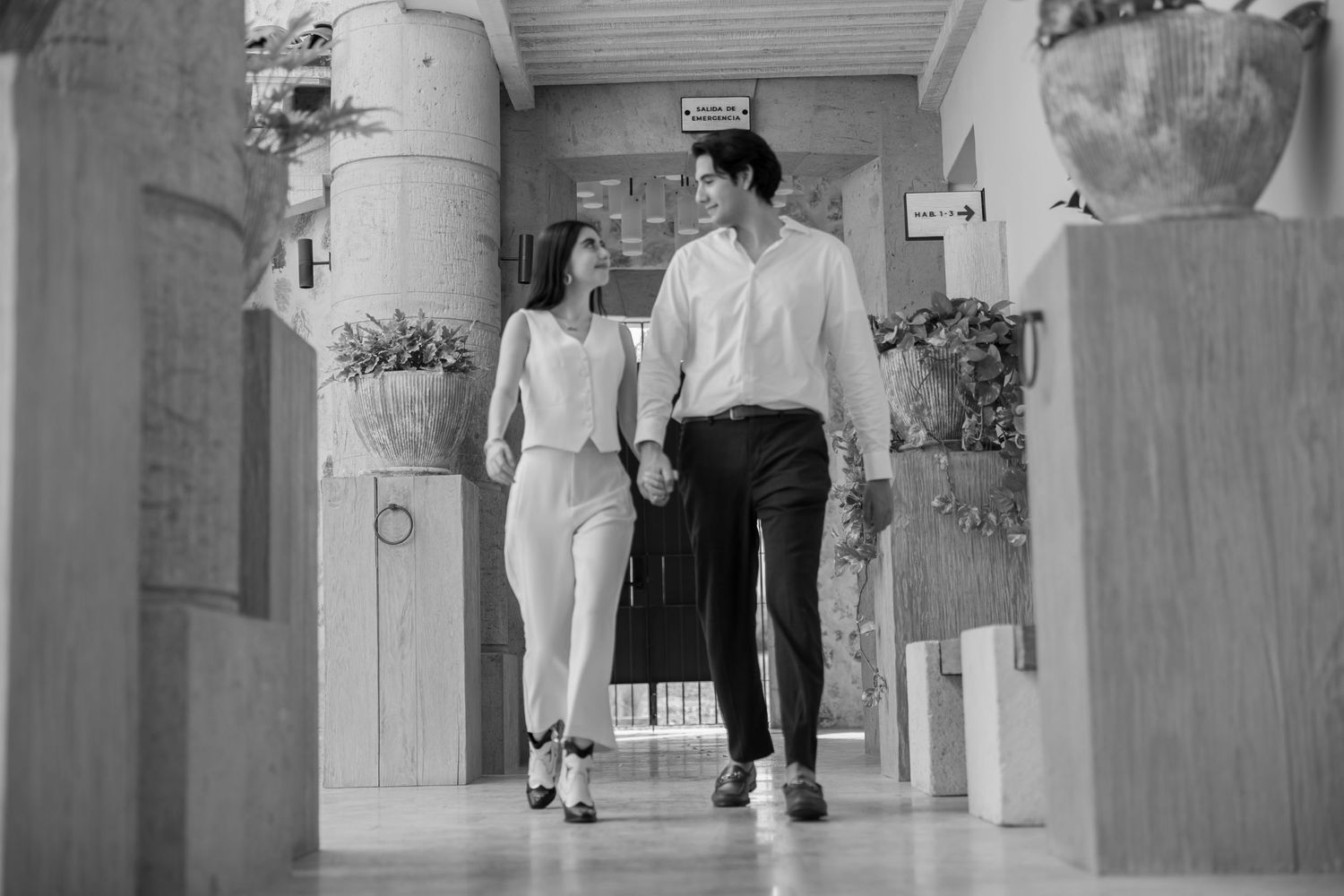 A couple in coordinated outfits walks together down a hallway in black and white. Propuesta de matrimonio Parras, Fotografo