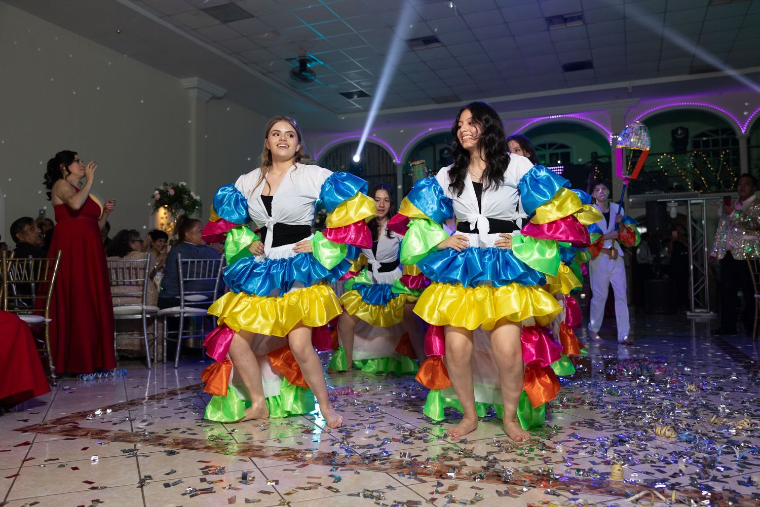Dance performers in matching multicolored ruffled costumes entertain at an indoor venue. Evento en Parras Coahuila , Fotógrafo Rulo