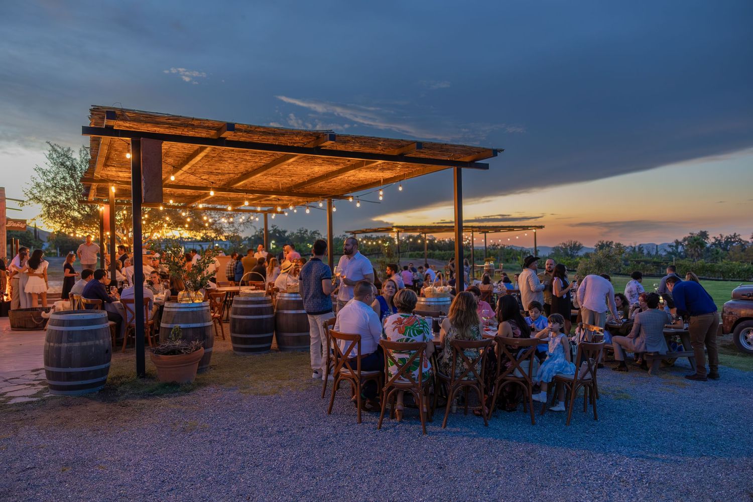 Outdoor dining area with wooden pergola and string lights at sunset with guests seated at tables. Boda en Parras Coahuila fotógrafo