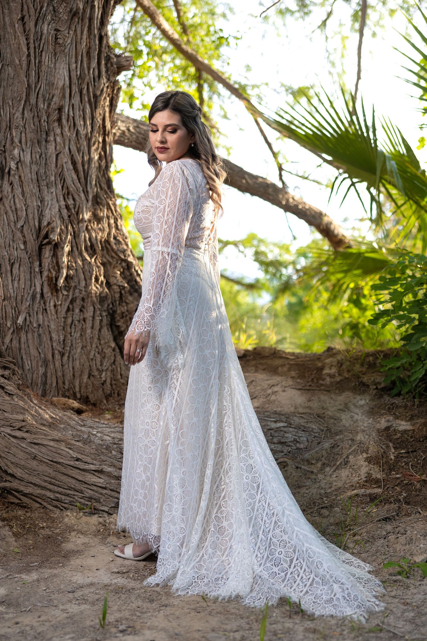 Detailed back view of intricate lace wedding gown with flowing train in natural setting. Sesión en Parras Coahuila