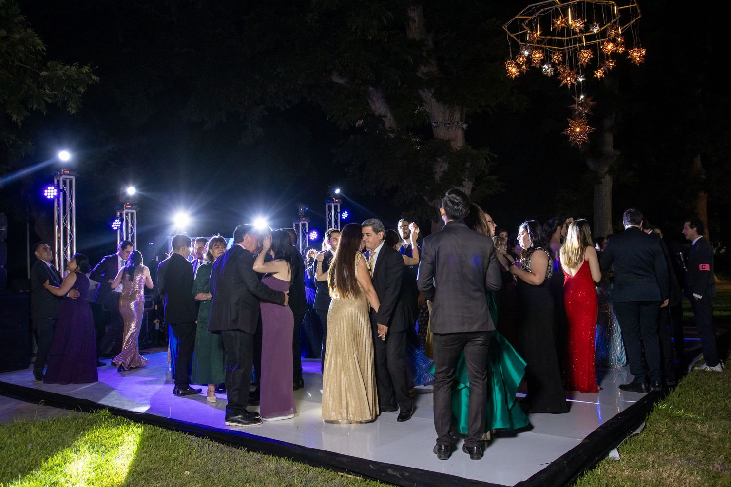 Party guests dance on an illuminated outdoor dance floor at night under string lights. Boda en Parras Coahuila, Fotógrafo de bodas