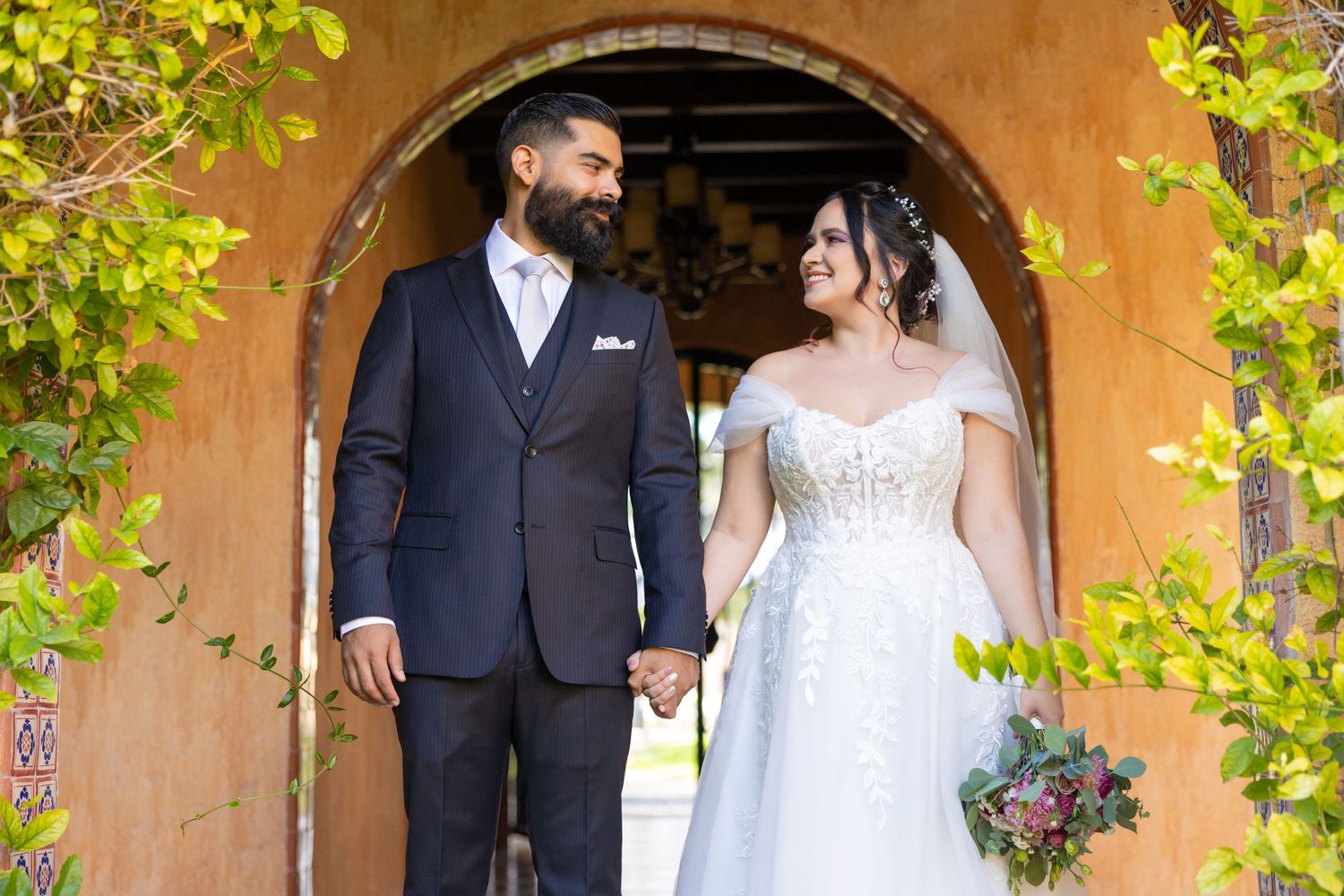 A elegant wedding couple poses under a terracotta archway with greenery. Boda en Parras Coahuila, Fotógrafo de bodas