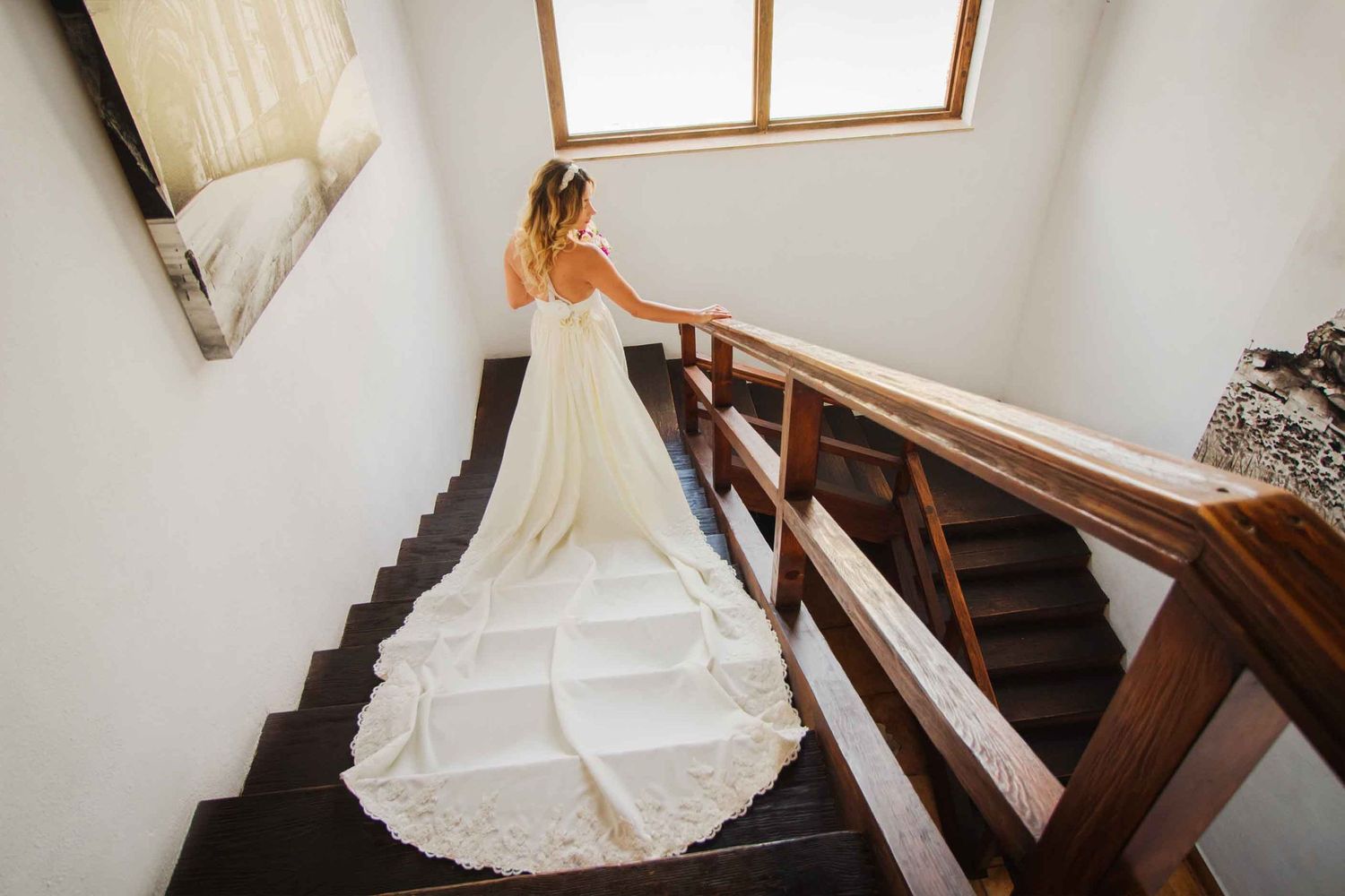 A flowing white wedding dress train descends a dark wooden staircase in an elegant interior setting. boda en Parras Coahuila fotógrafo
