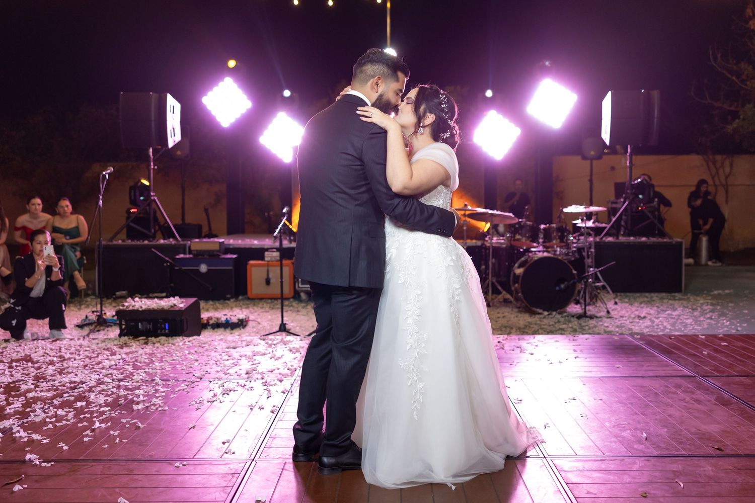 A couple shares their first dance as newlyweds under purple lighting with rose petals scattered on the dance floor. Boda en Parras Coahuila,