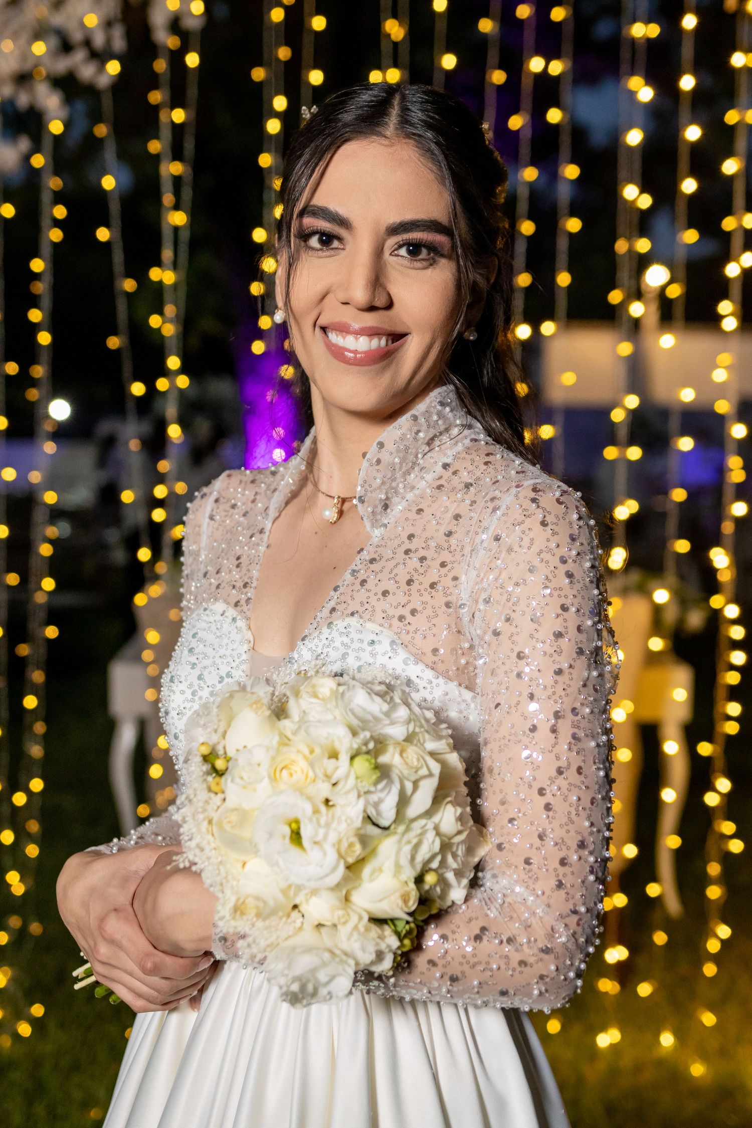 A wedding portrait featuring an elegant white gown with sheer beaded sleeves against sparkling lights. Boda en Parras Coahuila, Fotógrafo