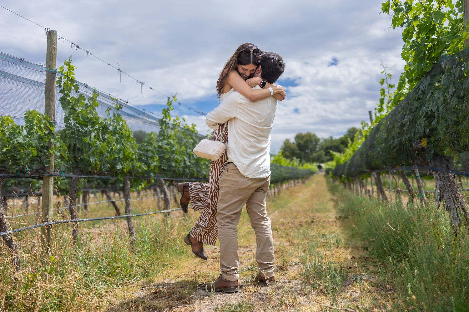 A romantic moment between two people embracing in a vineyard on a cloudy day.