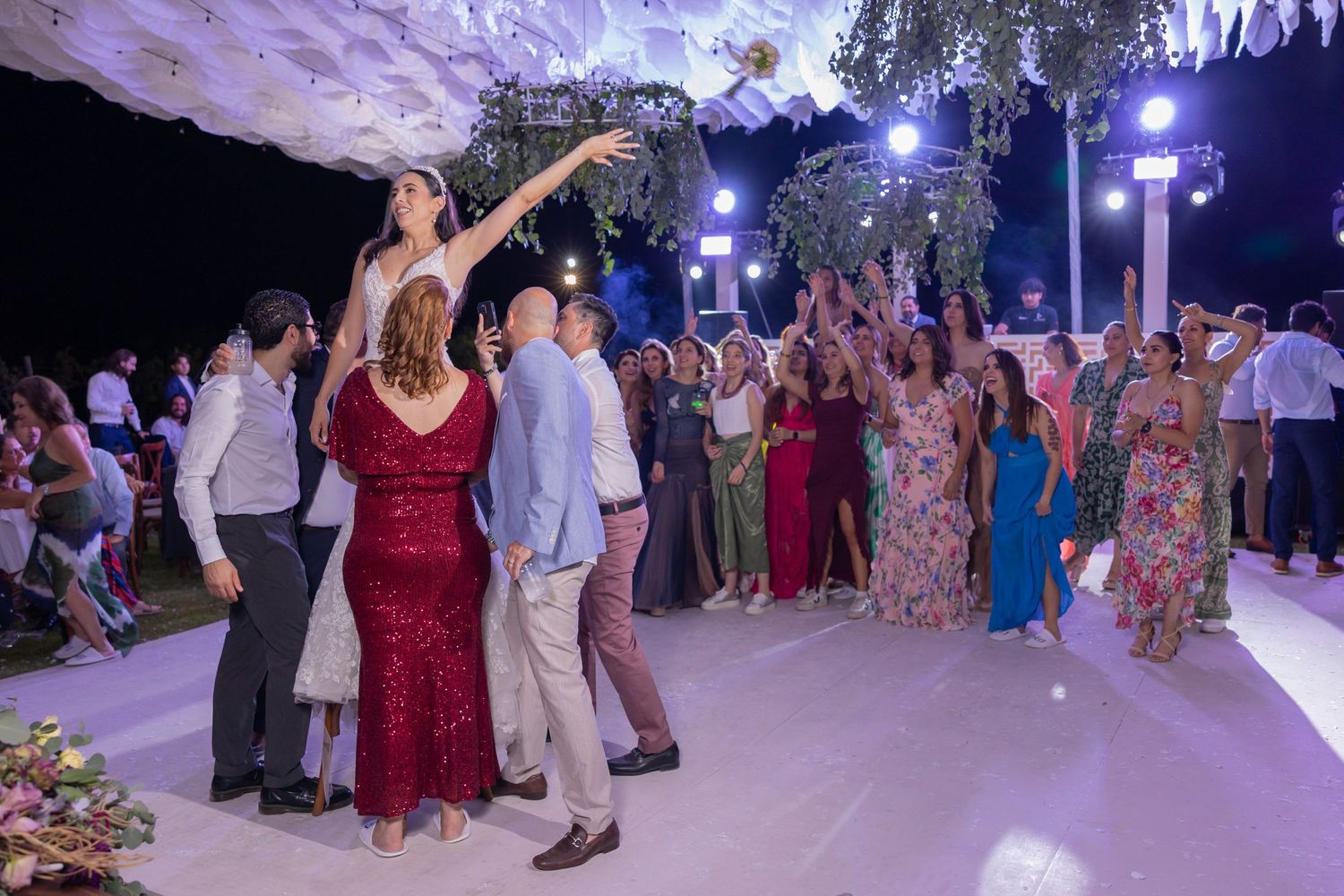 Wedding guests dance and celebrate on an illuminated outdoor dance floor under decorative hanging foliage. Boda en Parras Coahuila fotógrafo