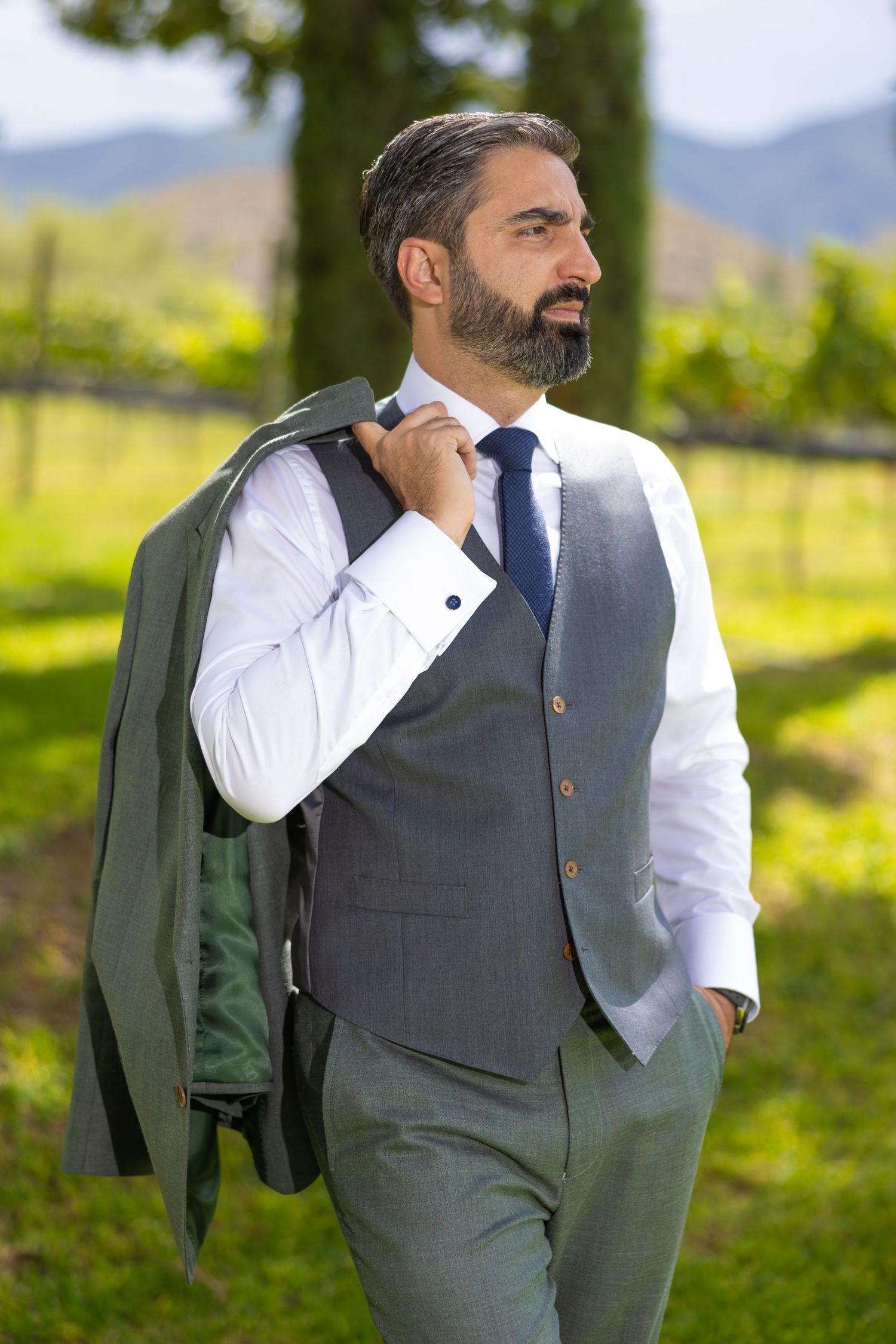 Well-dressed man in grey vest and white shirt carries green jacket over shoulder in vineyard setting. Boda en Parras Coahuila fotógrafo