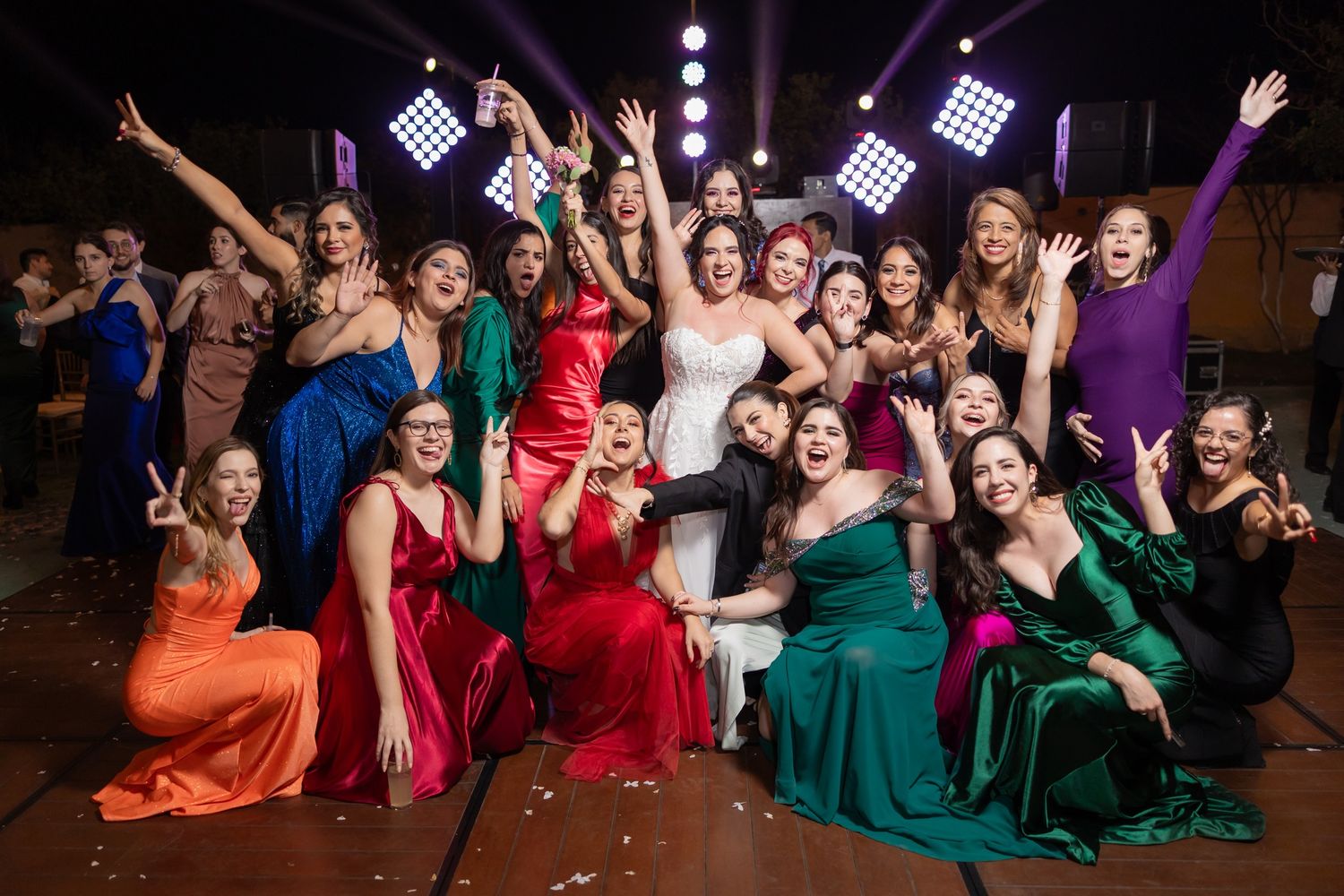 A festive group of wedding guests in colorful formal dresses celebrating on a dance floor. Boda en Parras Coahuila fotógrafo