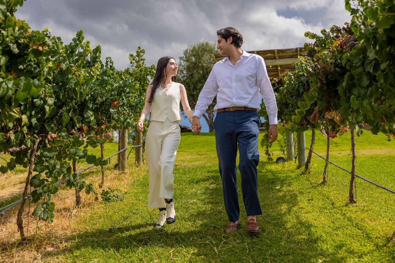 A couple holds hands while walking through a scenic vineyard on a cloudy afternoon. Propuesta de matrimonio Parras, Fotografo