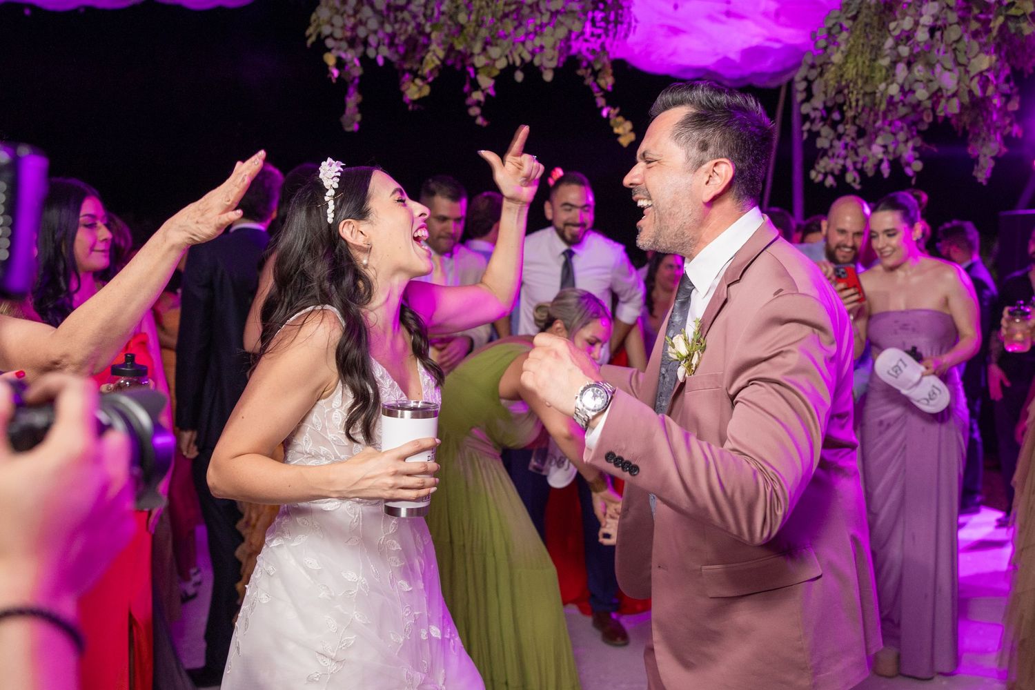 Couple celebrating on dance floor under purple lighting with wedding guests cheering in background. Boda en Parras Coahuila fotógrafo