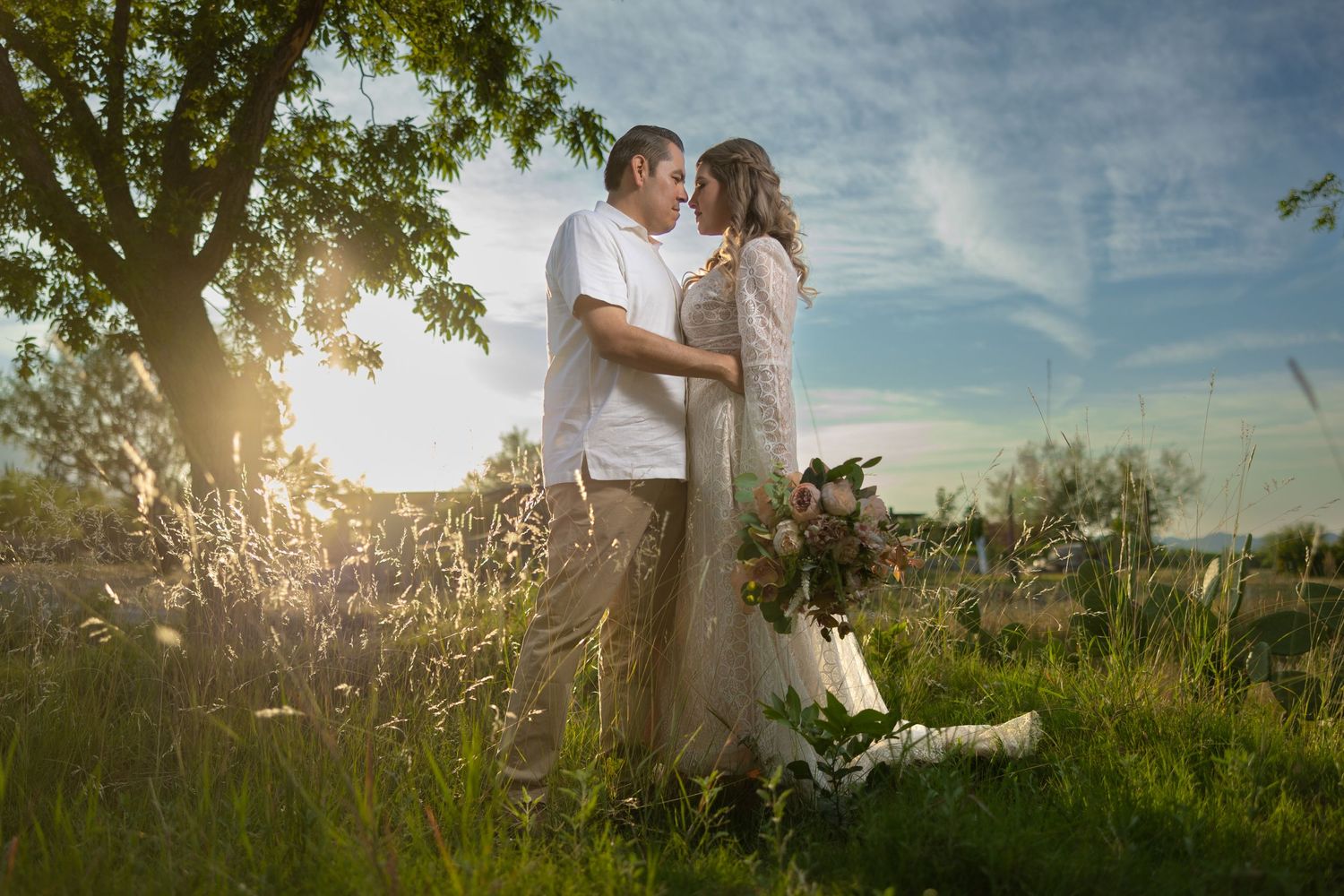 A couple sharing an intimate moment in a sunlit meadow beneath a tree.