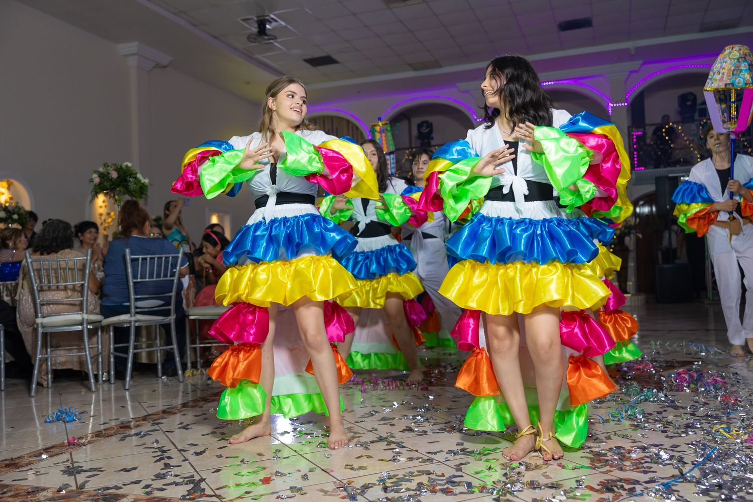 Two dancers in colorful tiered dresses perform a choreographed routine on a confetti-covered floor. Evento en Parras Coahuila , Fotógrafo