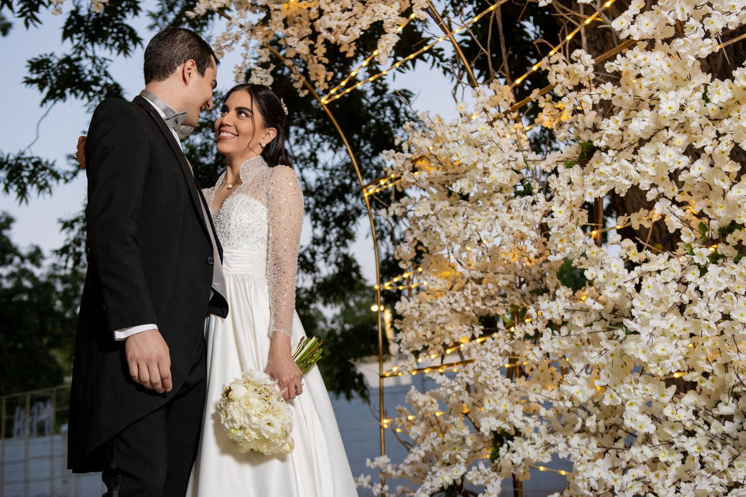Couple in wedding attire stands near blooming cherry blossom tree during spring celebration. Boda en Parras Coahuila, Fotógrafo de bodas
