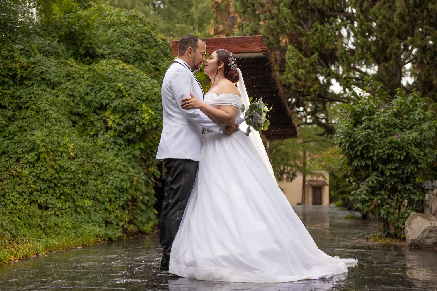 A couple in wedding attire embraces while dancing in a garden setting during their celebration.