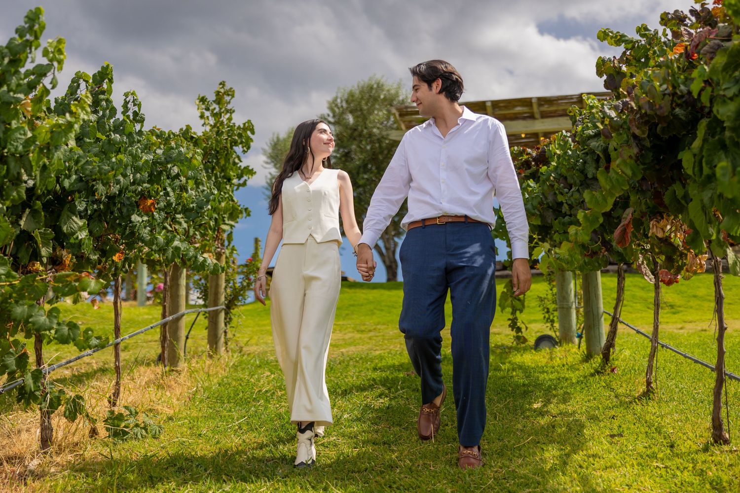 A couple walks together along grassy paths between vineyard rows under stormy skies. Propuesta de matrimonio Parras, Fotografo