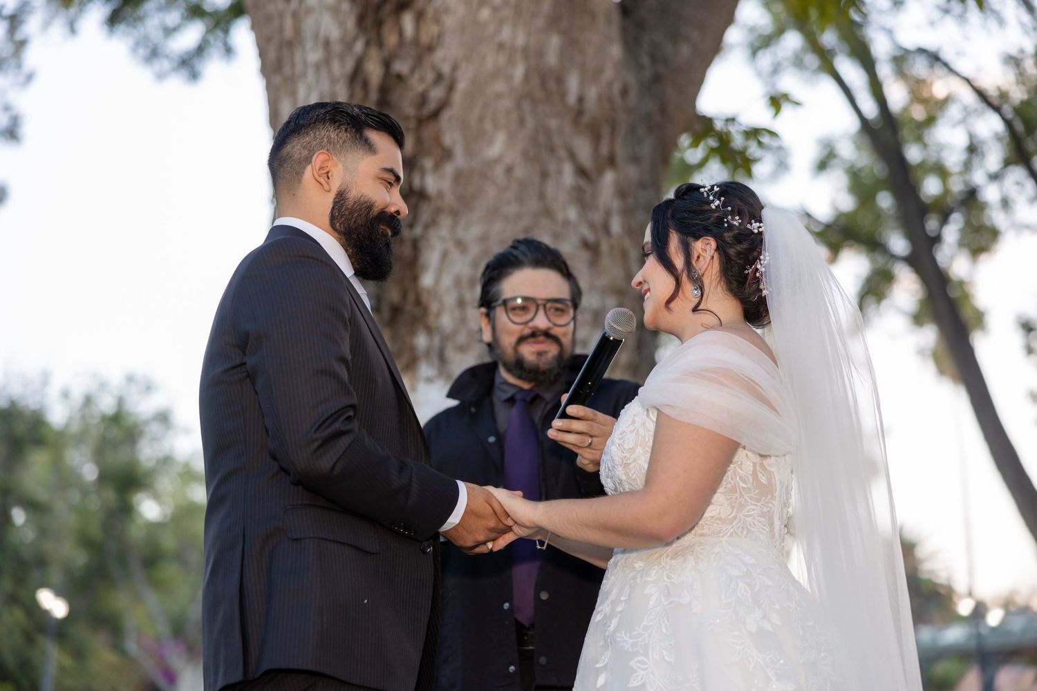 Wedding ceremony taking place under large tree with officiant and couple exchanging vows. Boda en Parras Coahuila, Fotógrafo de bodas