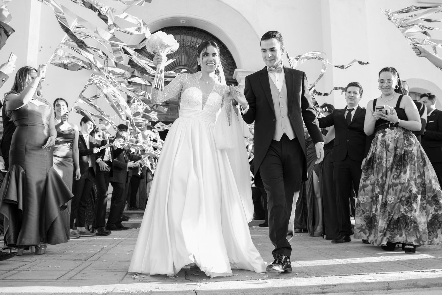 Wedding couple exits under a shower of paper streamers with guests cheering at elegant archway. Boda en Parras Coahuila, Fotógrafo de bodas