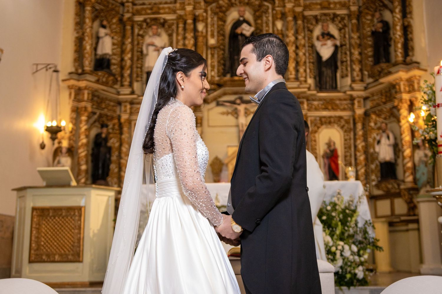 A couple shares an intimate moment during their wedding ceremony in front of a golden church altar. Boda en Parras Coahuila, Fotógrafo de bo