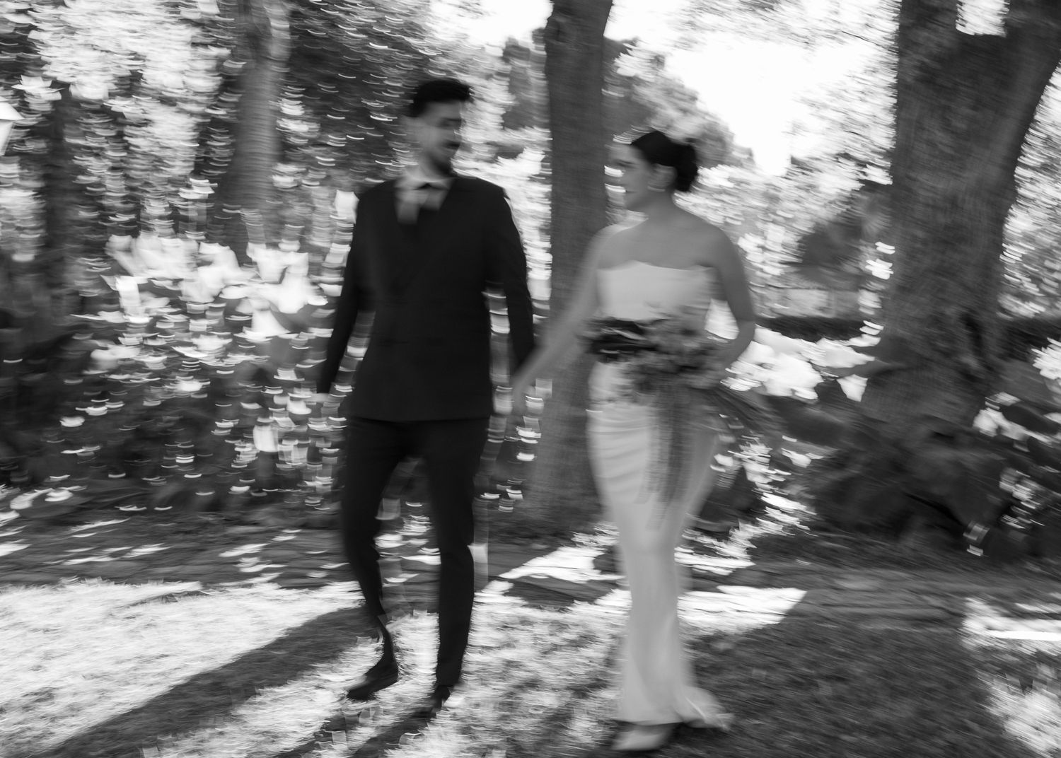 A black and white wedding photo series showing a couple walking and dancing together in a wooded outdoor setting.