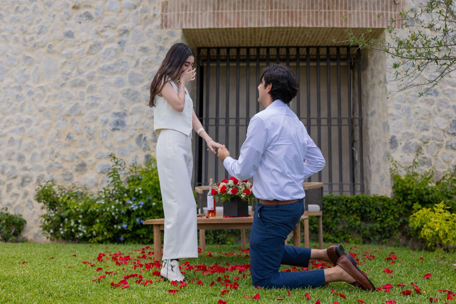 A romantic proposal scene with rose petals on grass against a stone wall backdrop. Propuesta de matrimonio Parras, Fotografo