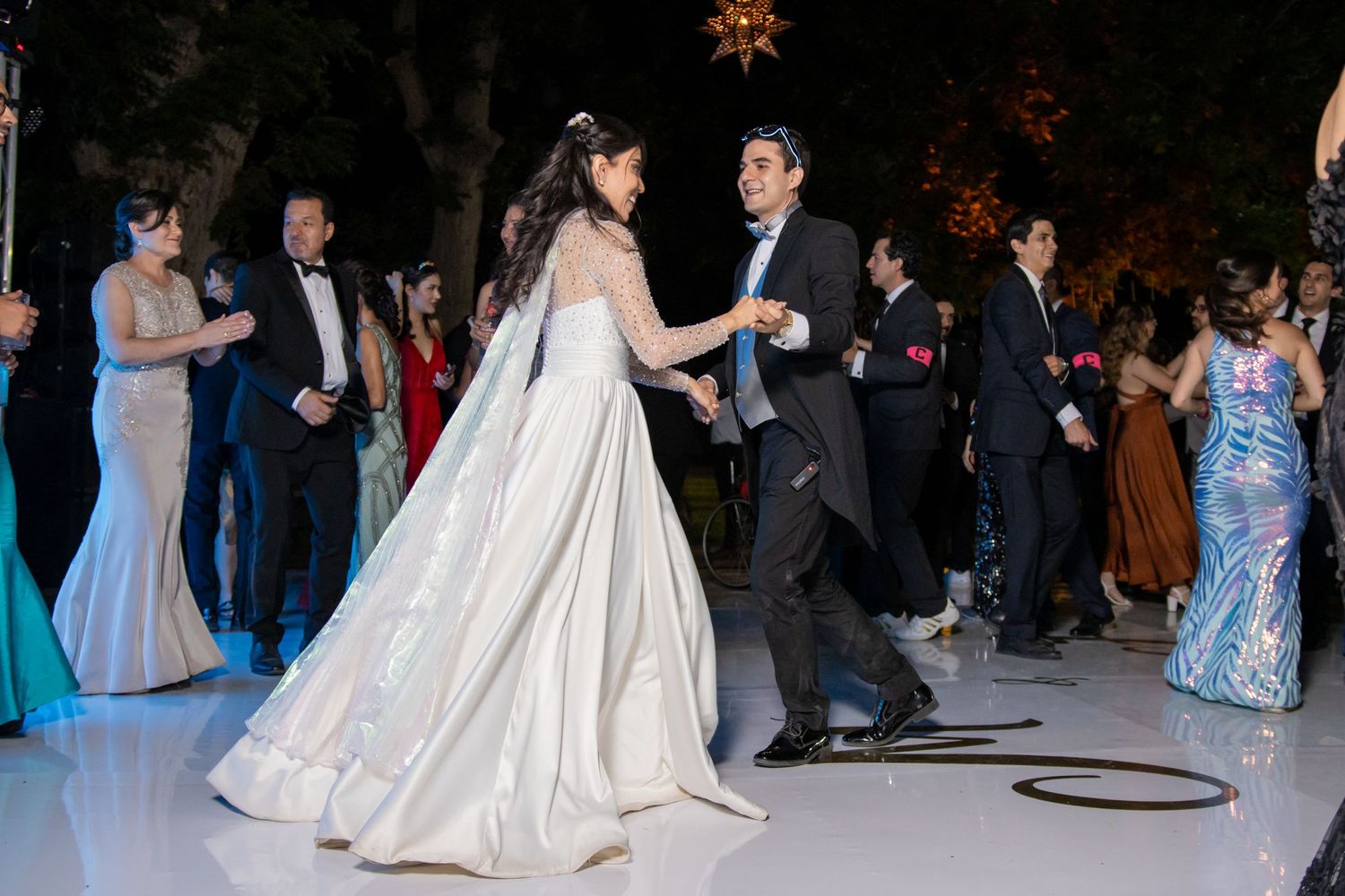 Wedding guests in formal attire gather around a white dance floor during evening celebrations. Boda en Parras Coahuila, Fotógrafo de bodas