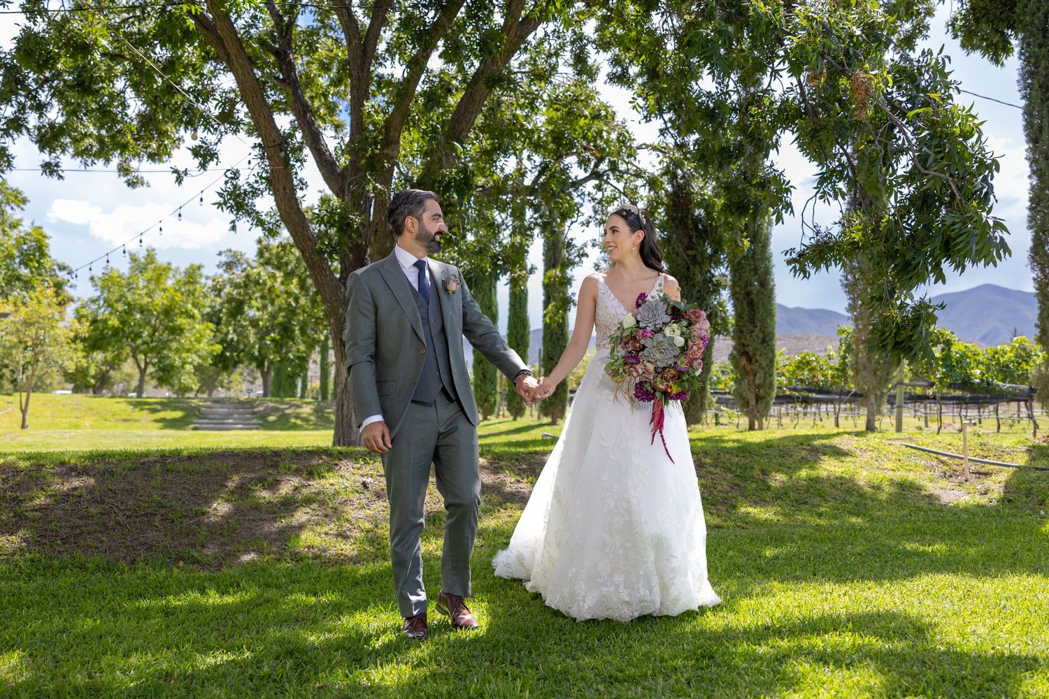 A wedding photo on lush green grass with trees and mountains in the background. Boda en Parras Coahuila fotógrafo