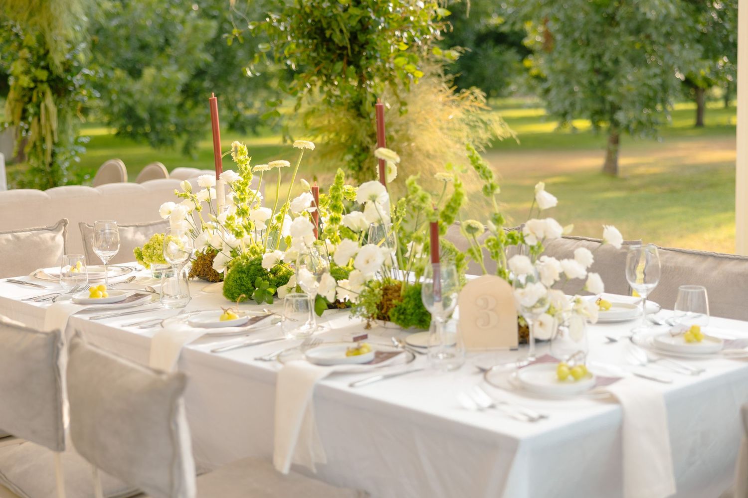 Outdoor wedding reception tables set with white linens and floral centerpieces in a sunny garden setting.