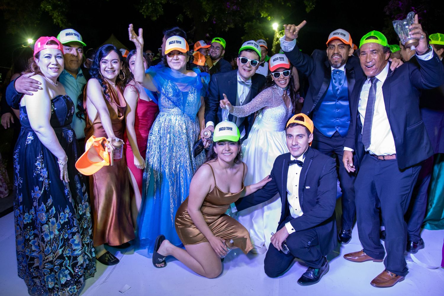 Party guests pose in formal attire and neon baseball caps during nighttime celebration. Boda en Parras Coahuila, Fotógrafo de bodas