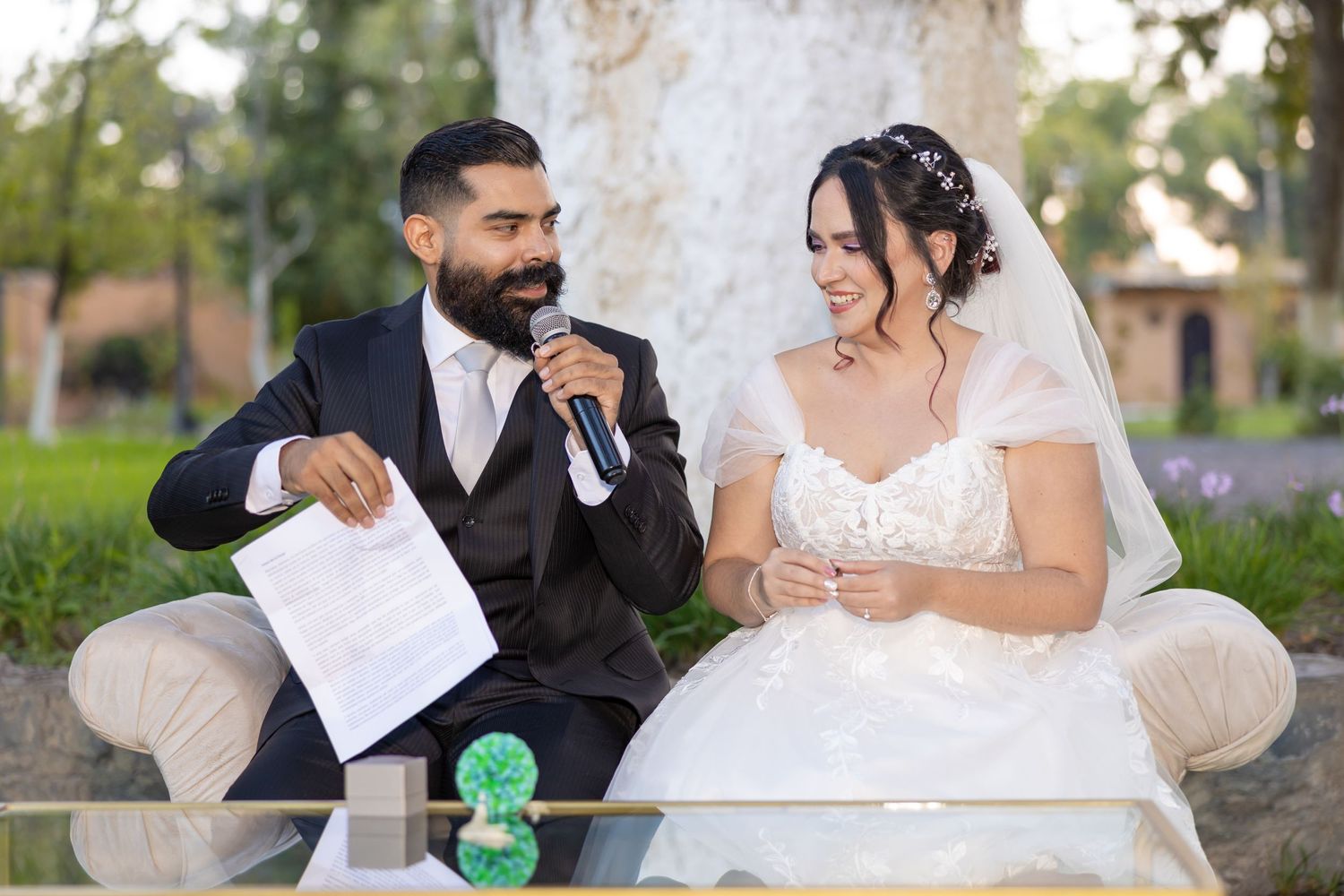 Bride in white dress and groom in dark suit sit together reading documents during outdoor ceremony. Boda en Parras Coahuila, Fotógrafo