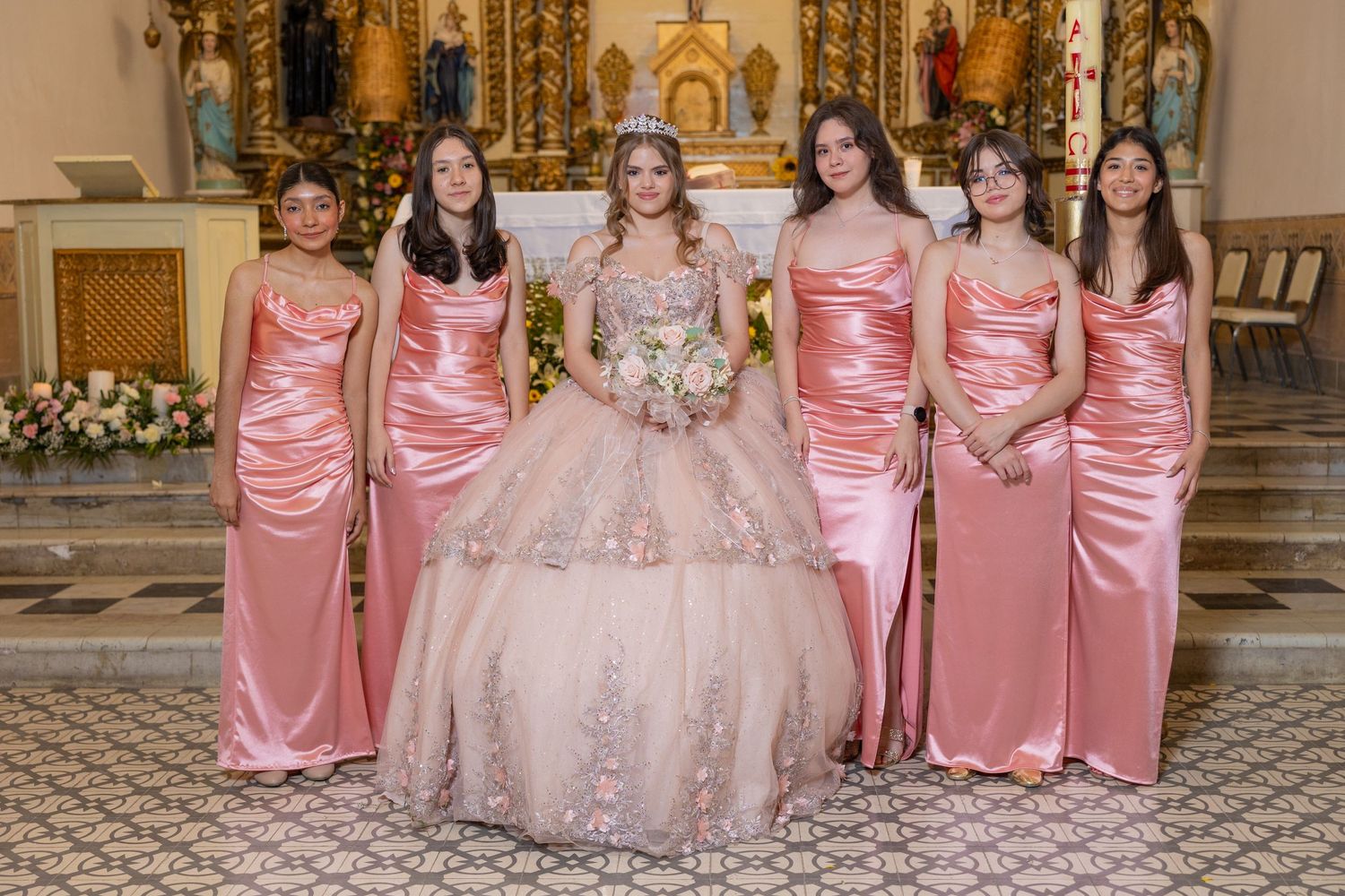 Bridesmaids in pink satin dresses pose with the celebrant in a grand church setting. Evento en Parras Coahuila , Fotógrafo Rulo