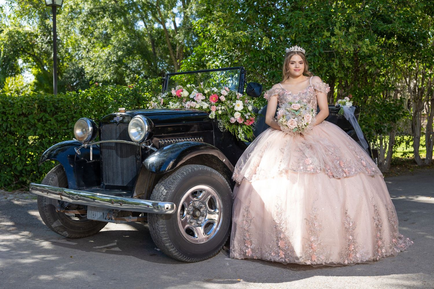 Pink ballgown celebration photo with vintage black car decorated with flowers in outdoor setting. Evento en Parras Coahuila , Fotógrafo Rulo