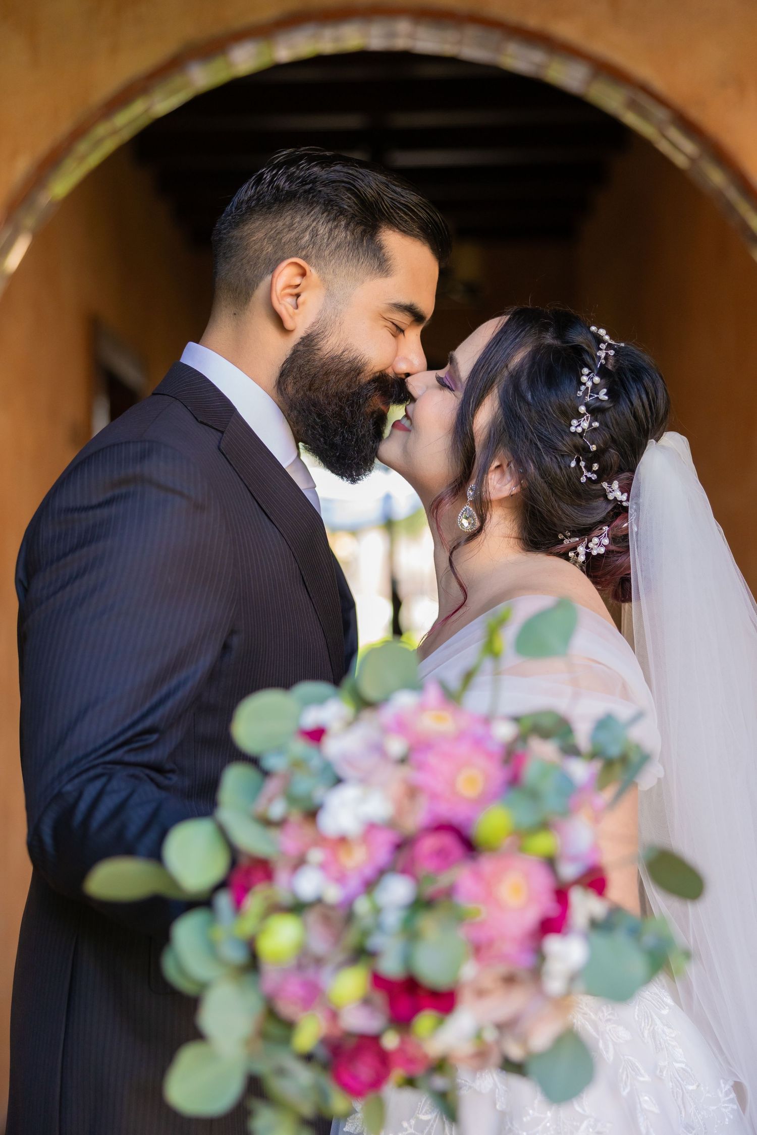 A tender wedding moment with a vibrant pink and green bouquet under an archway. Boda en Parras Coahuila, Fotógrafo de bodas