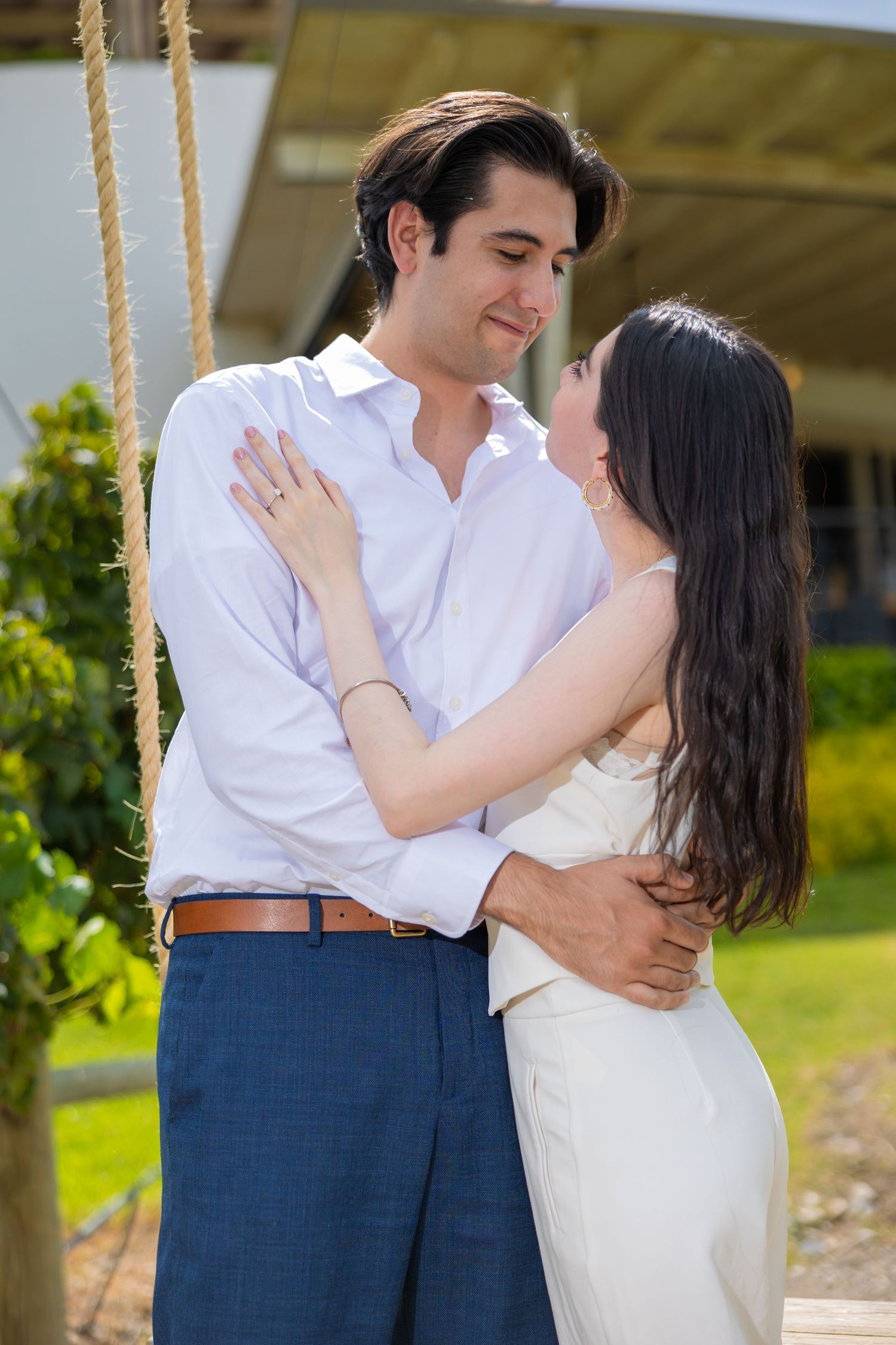 A romantic couple embraces in a garden setting, with her wearing white and him in a crisp button-down shirt. Propuesta de matrimonio Parras,