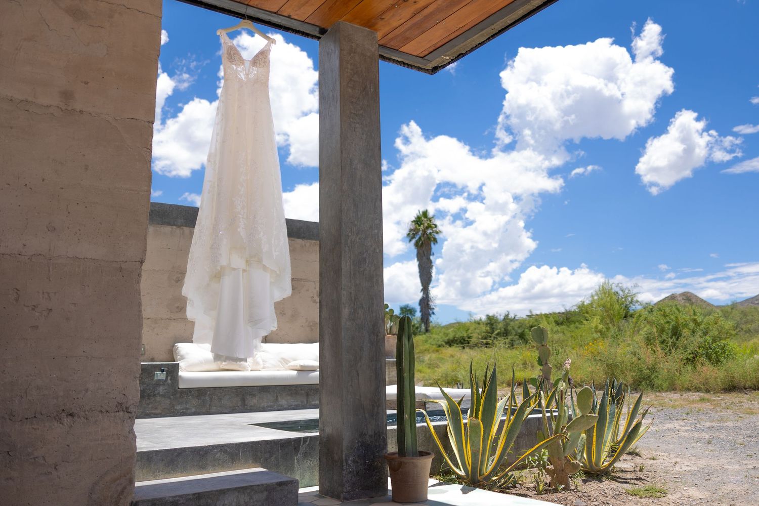 White wedding dress hanging in a desert venue with cacti and blue sky. Boda en Parras Coahuila fotógrafo