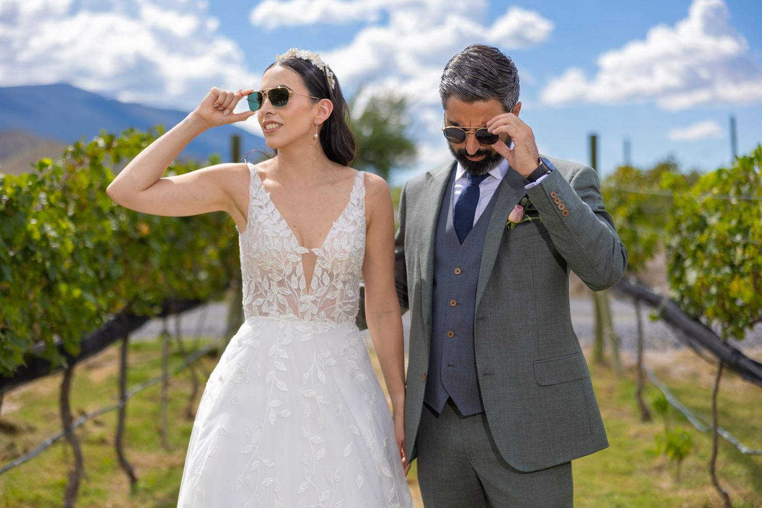 Wedding couple wearing sunglasses pose playfully in vineyard rows under blue sky. Boda en Parras Coahuila fotógrafo