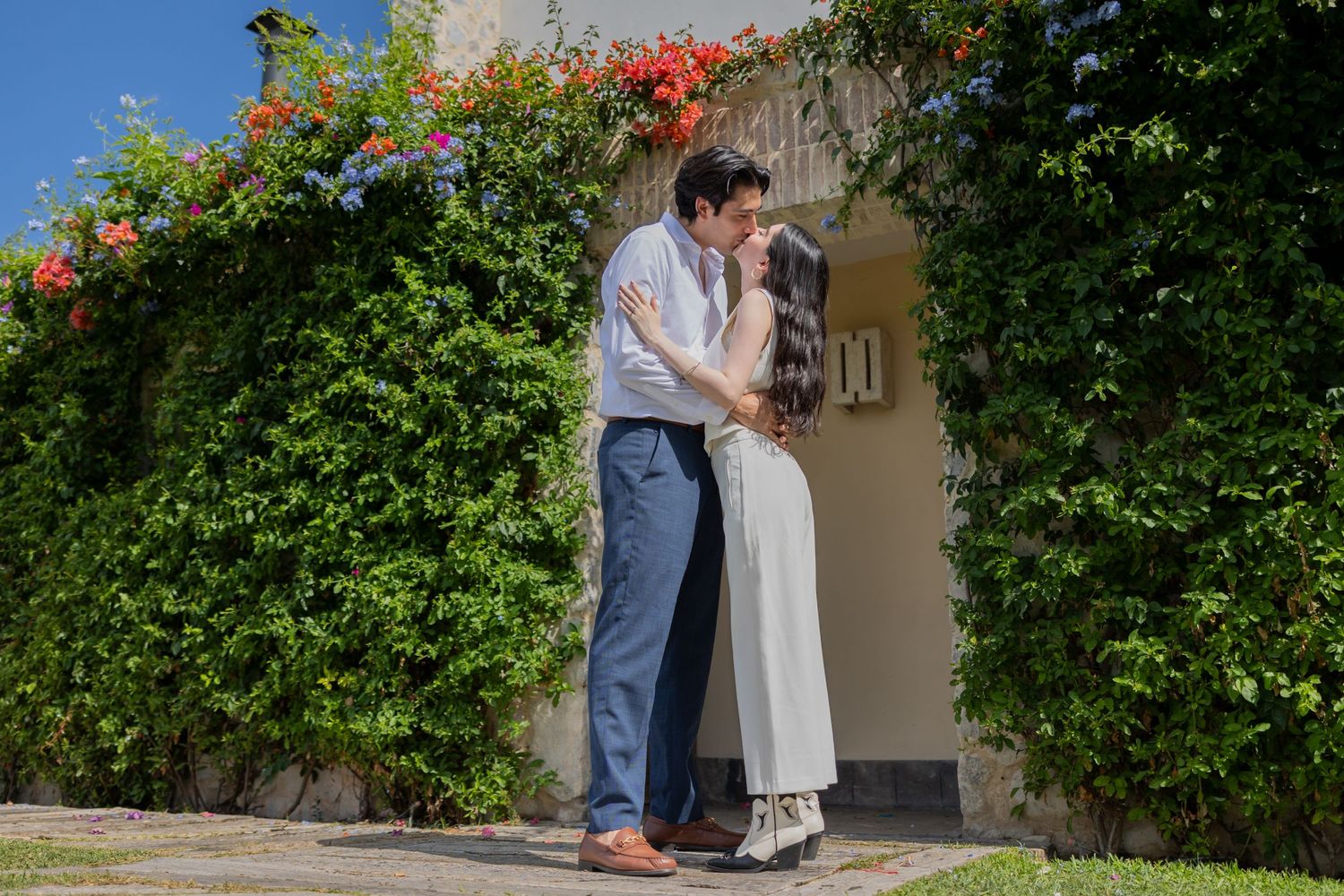 A tender moment between a couple standing beside a vine-covered wall with red flowers. Propuesta de matrimonio Parras, Fotografo