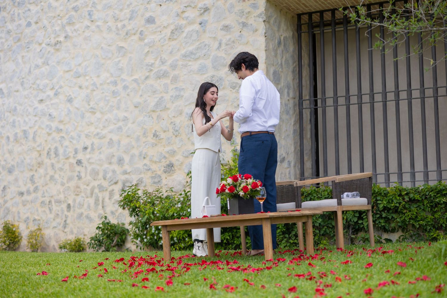 Two people share an intimate moment while standing on wooden benches with red petals below. Propuesta de matrimonio Parras, Fotografo