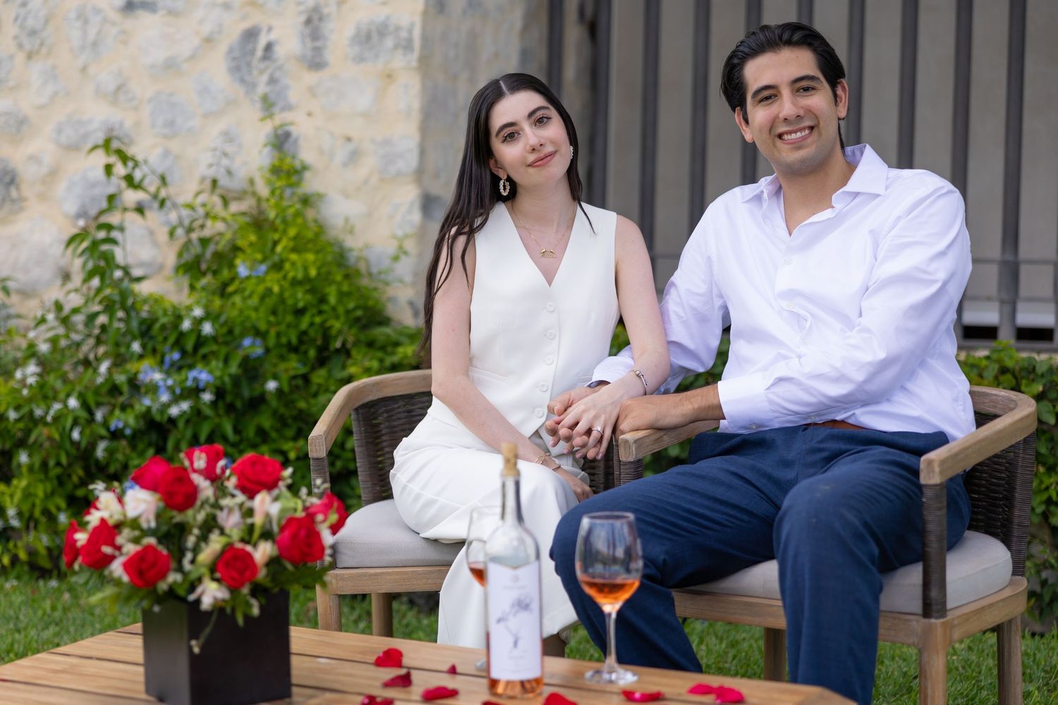 A couple enjoys drinks on a garden bench surrounded by red flowers and greenery. Propuesta de matrimonio Parras, Fotografo