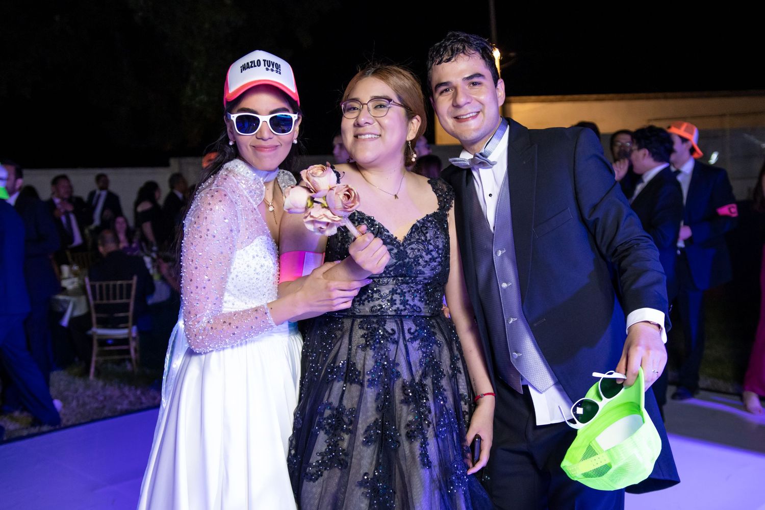 Wedding guests pose together wearing formal attire and colorful baseball caps at an evening celebration.Boda en Parras Coahuila