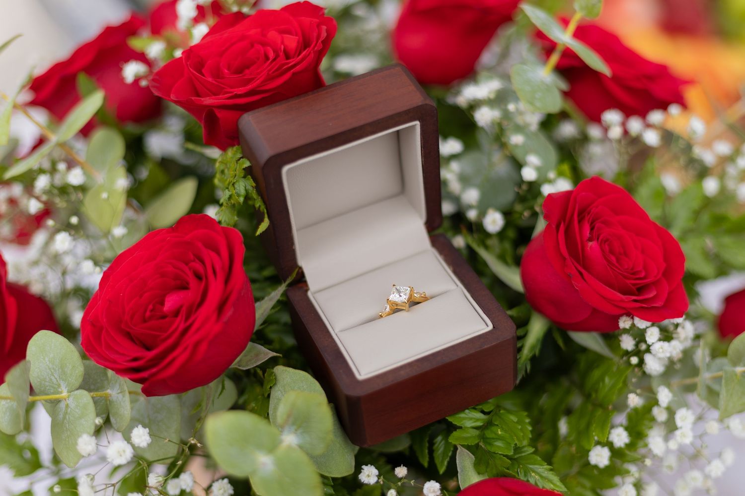 Diamond engagement ring in brown box surrounded by red roses and baby's breath flowers. boda en Parras Coahuila fotógrafo