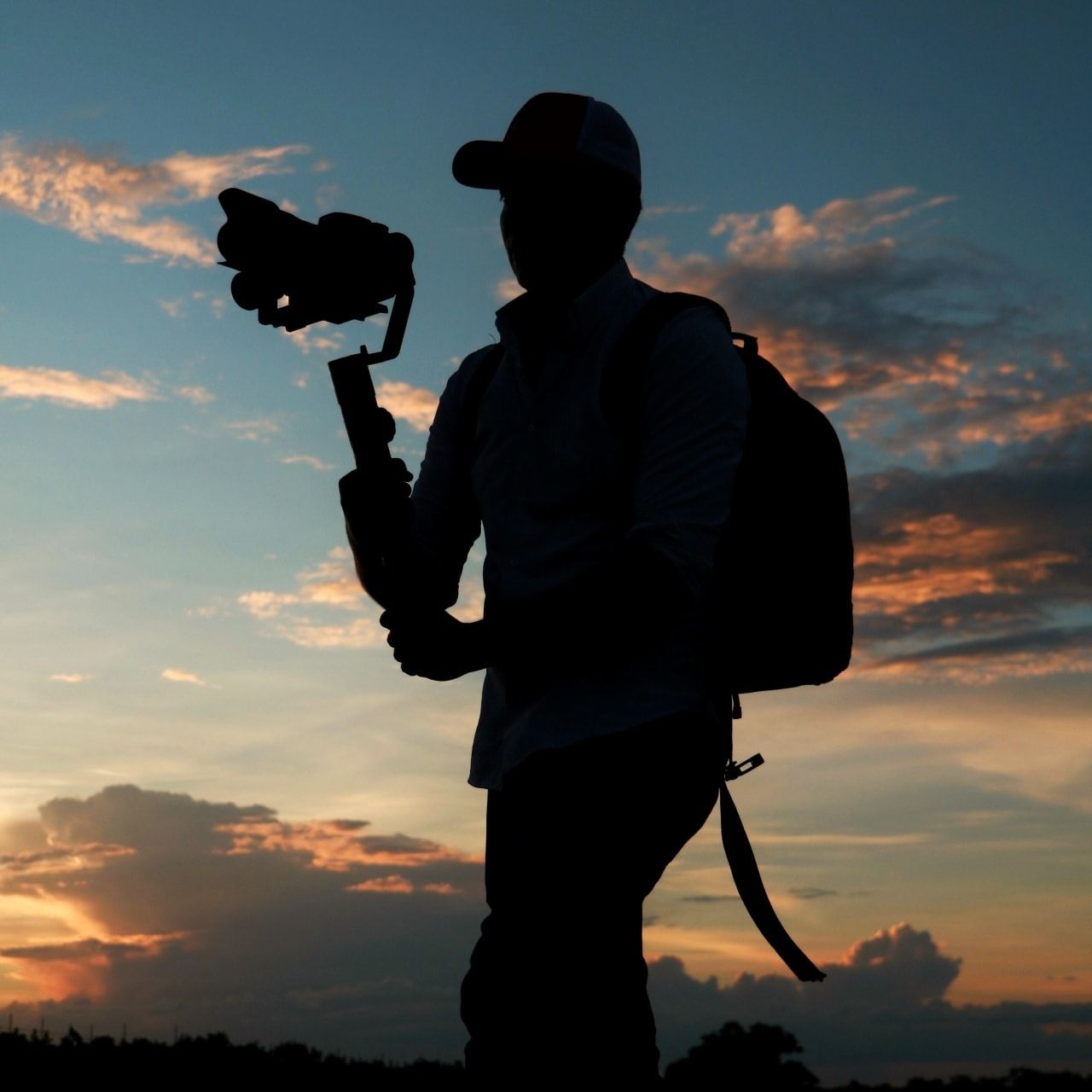 Silhouette of a photographer with camera gear against a dramatic sunset sky.
