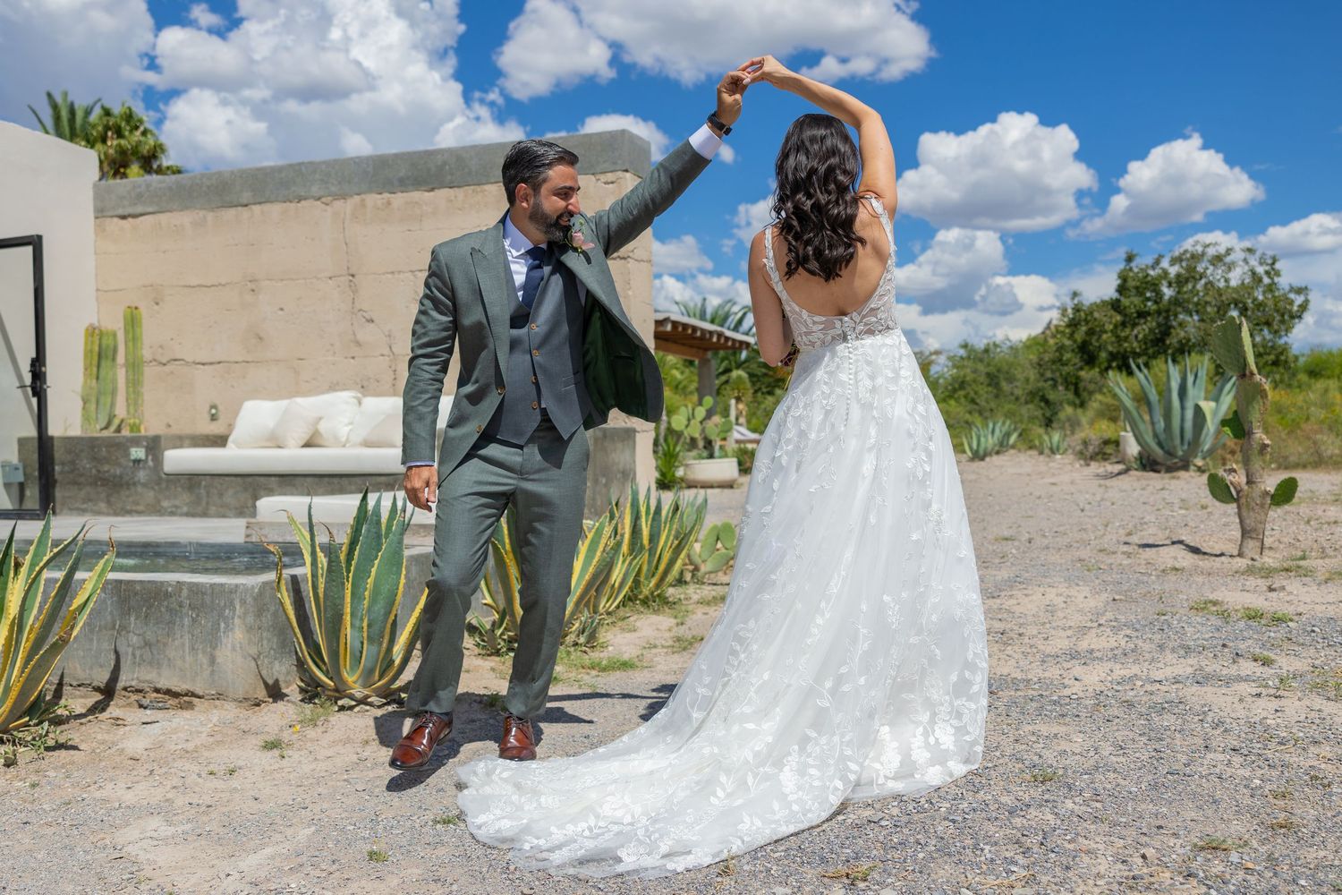 A couple in wedding attire dancing together in a desert landscape with agave plants and white clouds. Boda en Parras Coahuila fotógrafo