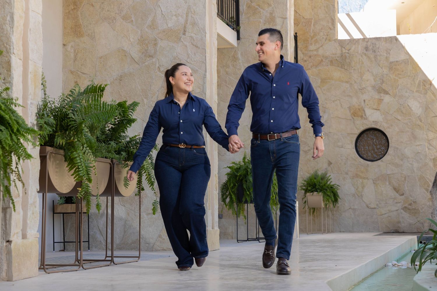 A couple in navy blue outfits running and playing together along a stone corridor with arches.
