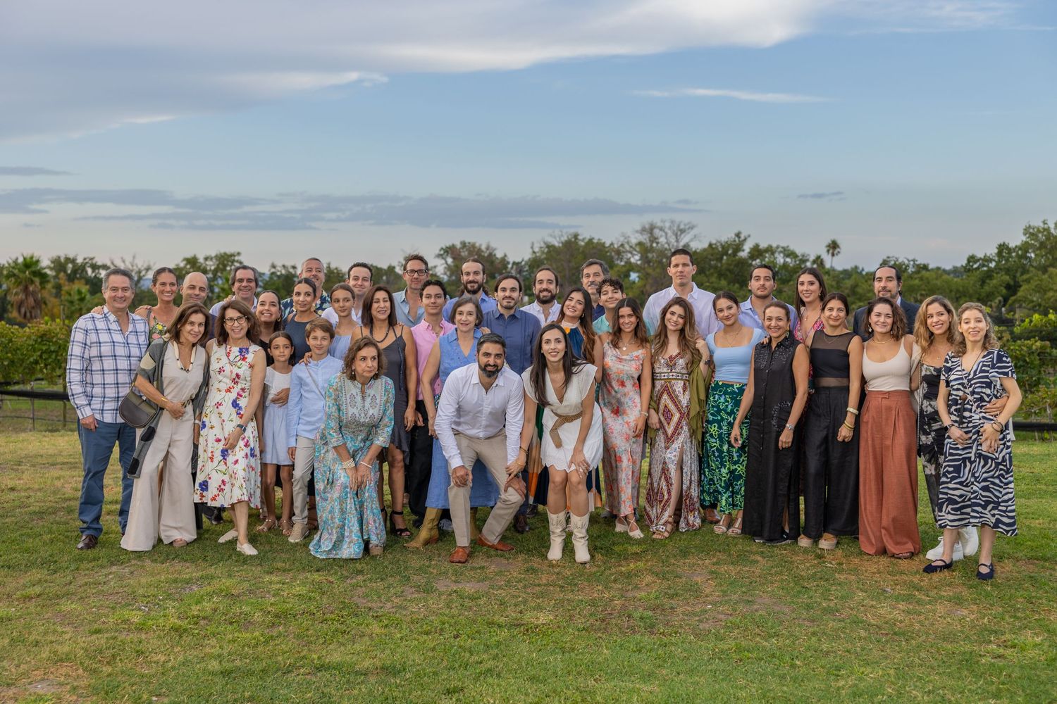 Large group photo of wedding guests gathered outdoors on a grassy hill under cloudy skies. Boda en Parras Coahuila fotógrafo