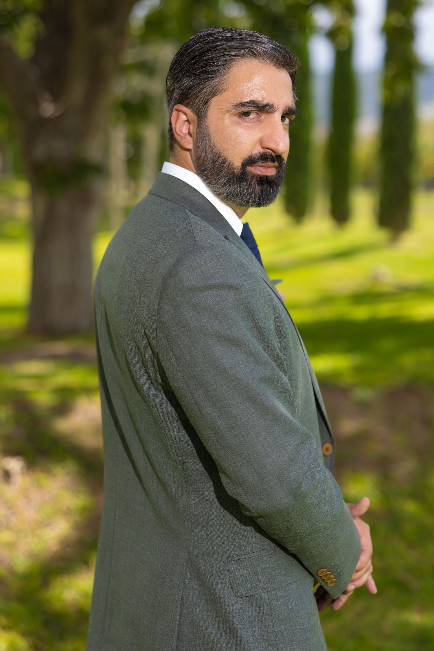 Portrait of a groom in a dark suit standing in a sun-dappled garden setting. Boda en Parras Coahuila fotógrafo