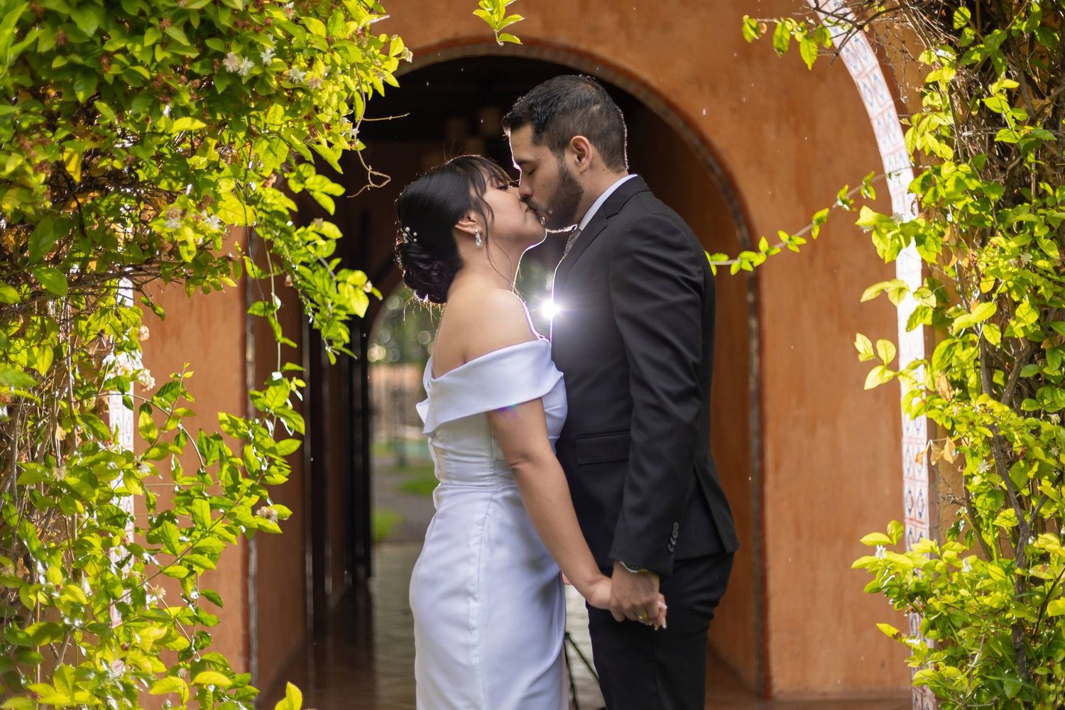 A romantic moment captured under an archway decorated with lush greenery. Boda en Parras Coahuila fotógrafo