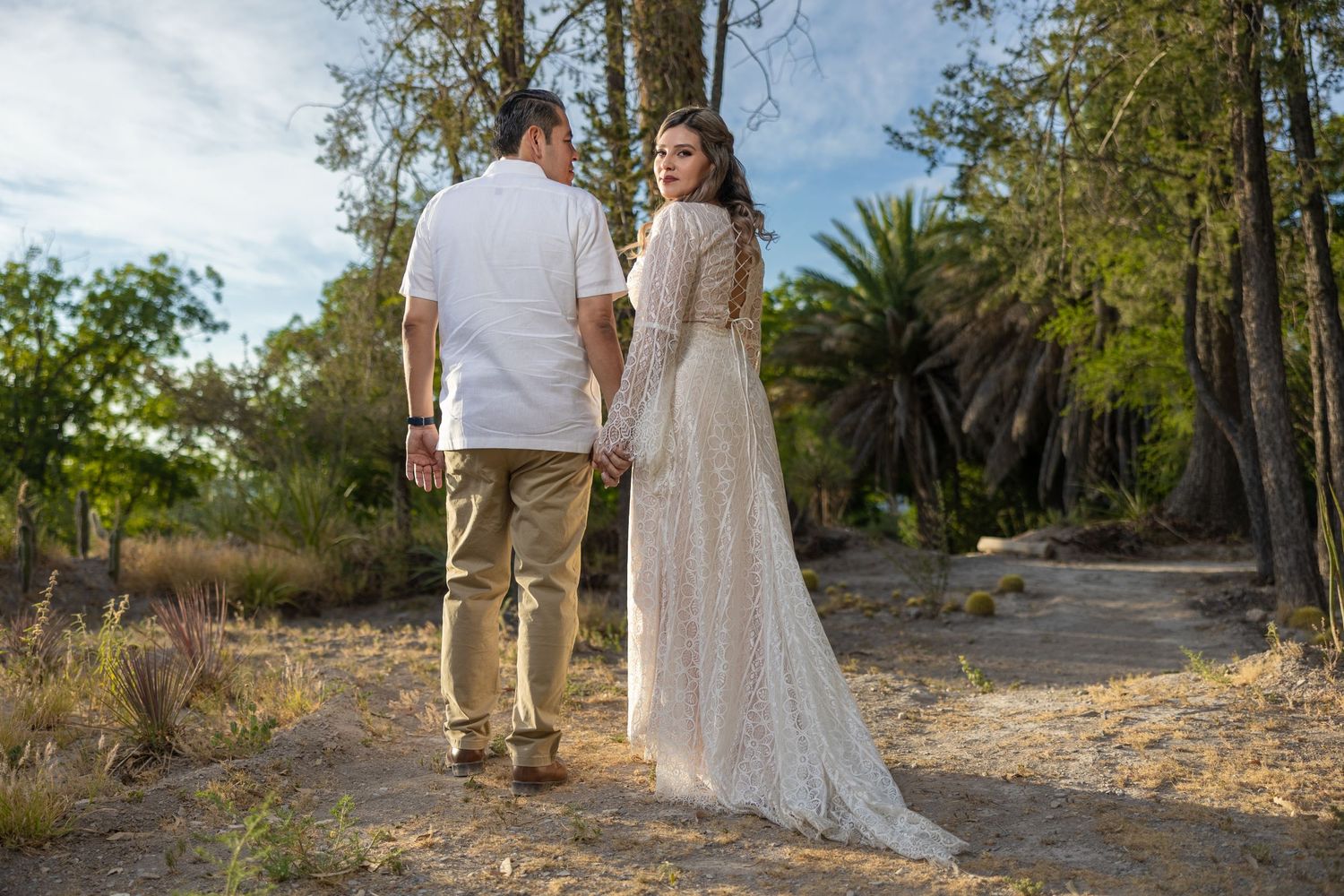 Wedding couple photographed from behind on rustic dirt path surrounded by greenery. Sesión en Parras Coahuila