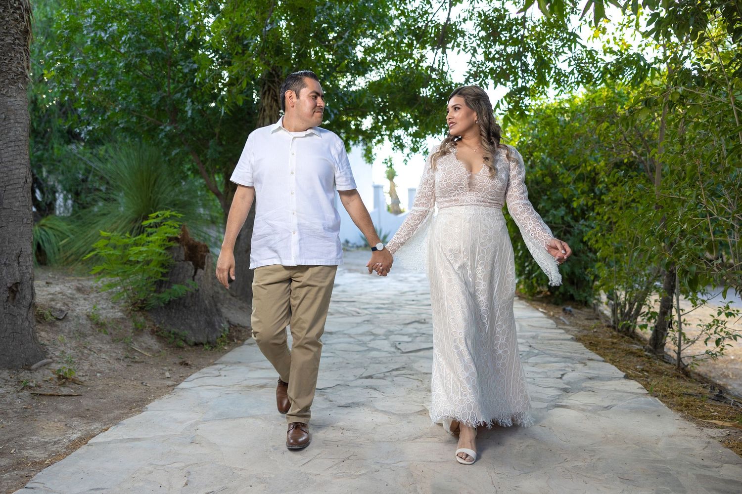 Couple walking hand in hand along garden path in wedding attire. Sesión en Parras Coahuila
