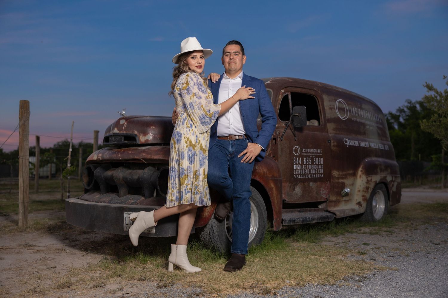 Stylishly dressed couple poses beside rustic vintage delivery truck at dusk. boda en Parras Coahuila fotógrafo